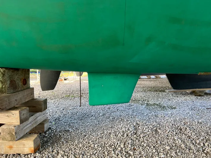 Trebuchet Yacht Photos Pics Green hull of a 2000 Switch 51 catamaran on gravel, supported by wooden blocks.