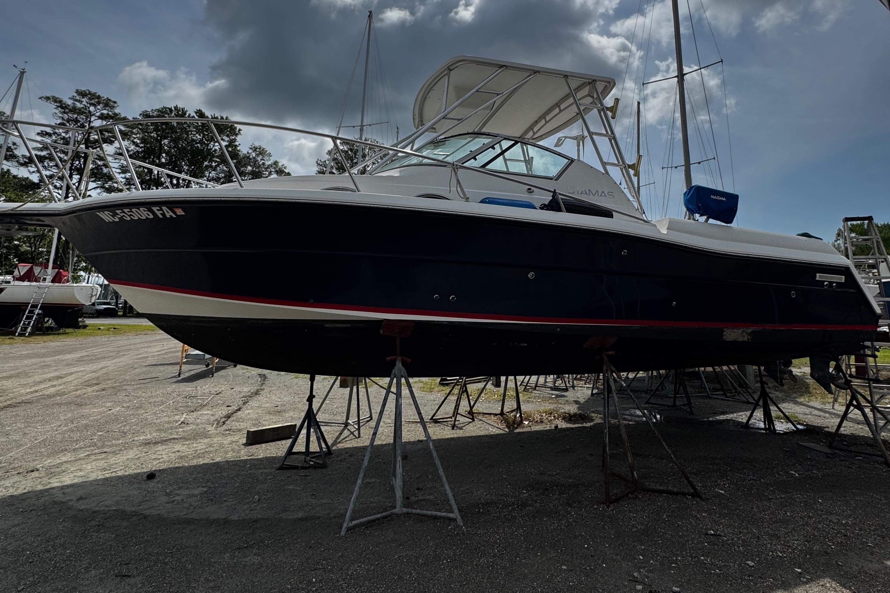 2001 Stamas 310 Express boat on stands, outdoor storage, cloudy sky background.