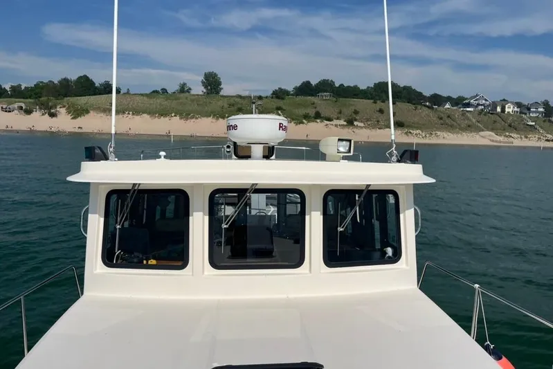 Nomad Yacht Photos Pics Nordic Tug 37 (2000) cruising near a sandy shoreline under a clear blue sky.