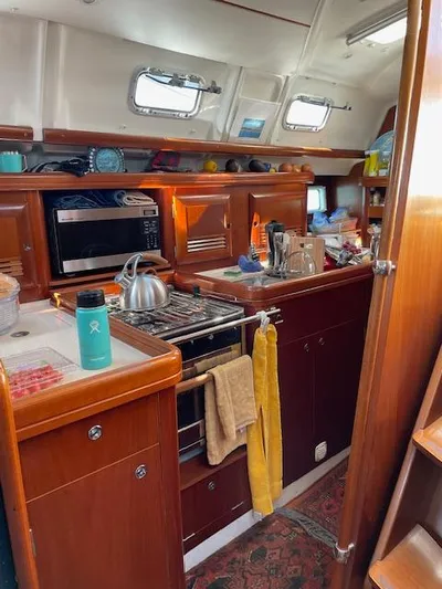 Peregrine Yacht Photos Pics Interior of a 2005 Beneteau 423 sailboat kitchen with wooden cabinetry and modern appliances.