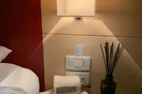 Modern hotel room nightstand with rolled towels, decorative vase, and soft lighting.