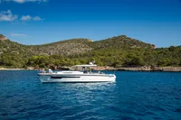 2022 Nimbus T11 boat cruising on clear blue water near a scenic, hilly coastline.