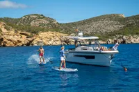 People paddleboarding near a 2022 Nimbus T11 boat in a scenic coastal area.