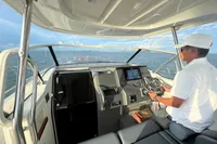 Person steering 2022 Nimbus T11 boat on open water, sunny day.