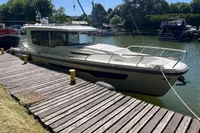 2024 Nimbus Commuter 11 docked at a sunny marina, surrounded by lush greenery.