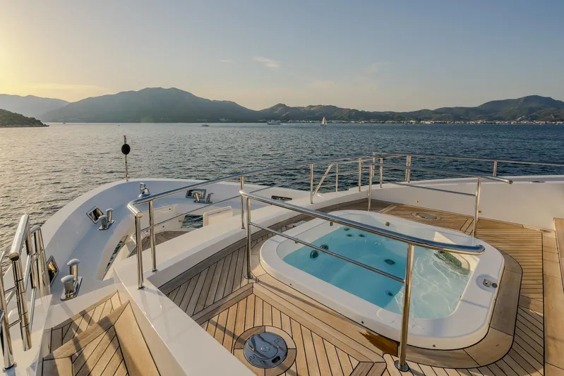 Charisma Yacht Photos Pics Luxurious Benetti Fast 125 yacht deck with jacuzzi, 2015 model, overlooking serene ocean and mountains.
