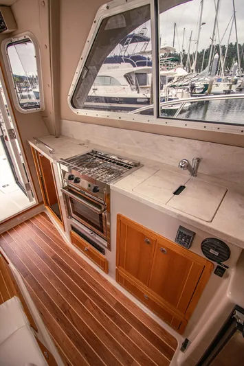Halcyon Yacht Photos Pics Compact kitchen in 2015 Aspen C100 boat with stove, sink, and wooden cabinets.