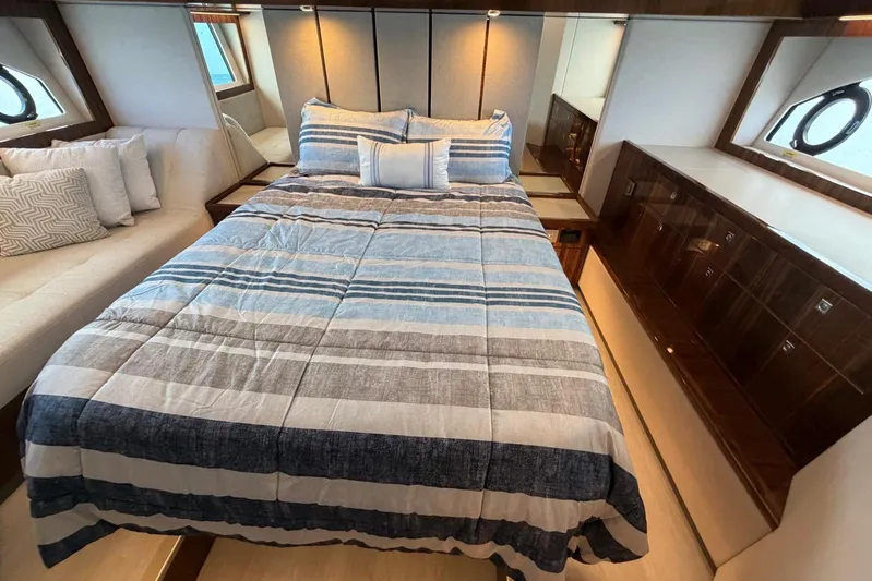  Yacht Photos Pics Luxurious bedroom interior of 2026 Riviera 505 SUV yacht with striped bedding and elegant wood finishes.