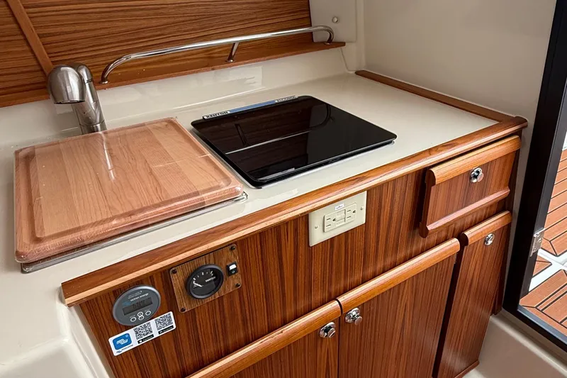  Yacht Photos Pics 2025 Ranger Tugs R-25 galley with wooden cabinetry, sink, and electric cooktop.
