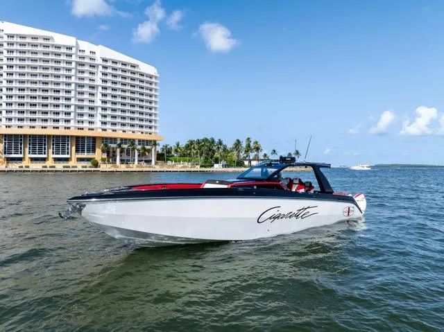  Yacht Photos Pics 2025 Cigarette 42 Auroris boat cruising near a waterfront building under a clear blue sky.