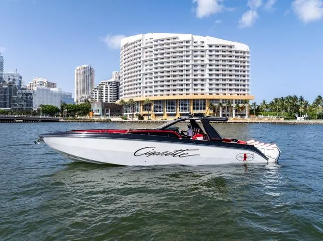  Yacht Photos Pics 2025 Cigarette 42 Auroris boat cruising near modern waterfront buildings under a clear blue sky.