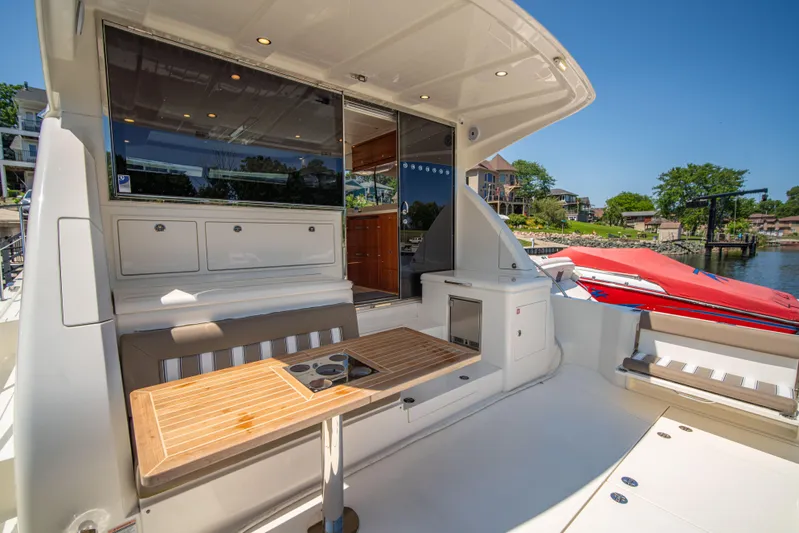  Yacht Photos Pics 2020 Riviera 525 SUV yacht with outdoor seating and table, docked by a scenic waterfront.