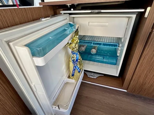 Sea Of Dreams Yacht Photos Pics Open refrigerator inside 2024 Beneteau Antares 9 boat, showing drinks and a bottle.