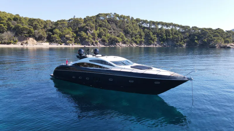 Low Profile Yacht Photos Pics 2007 Sunseeker Predator 82 yacht anchored in clear blue waters near a forested shoreline.