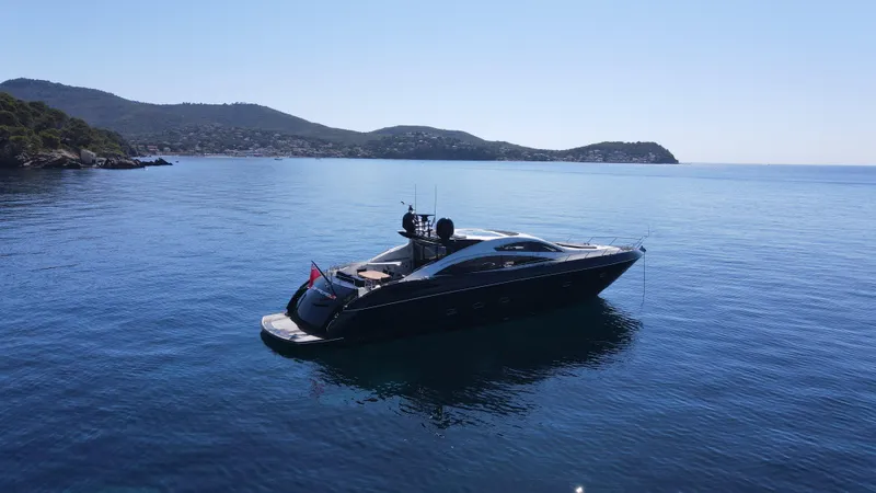 Low Profile Yacht Photos Pics 2007 Sunseeker Predator 82 yacht on calm blue waters with scenic hills in the background.