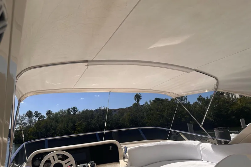 Splendor Yacht Photos Pics 2007 Azimut 55E yacht cockpit with canopy, featuring a steering wheel and lush greenery backdrop.