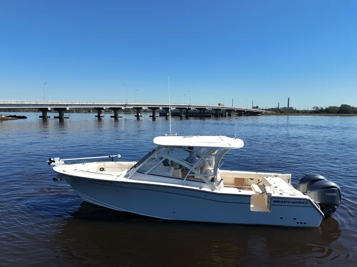  Yacht Photos Pics 2022 Grady-White Freedom 307 boat on calm water near a bridge under clear blue sky.