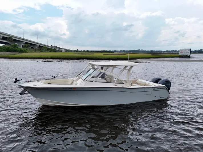  Yacht Photos Pics 2022 Grady-White Freedom 307 boat on water near a bridge, under cloudy sky.