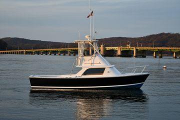 1965 Bertram Sportfisher boat on calm water near a bridge, scenic background.
