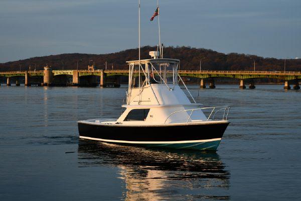 1965 Bertram Sportfisher boat on calm water near a bridge at sunset.