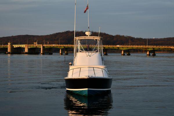 1965 Bertram Sportfisher boat on calm water near a bridge at sunset.