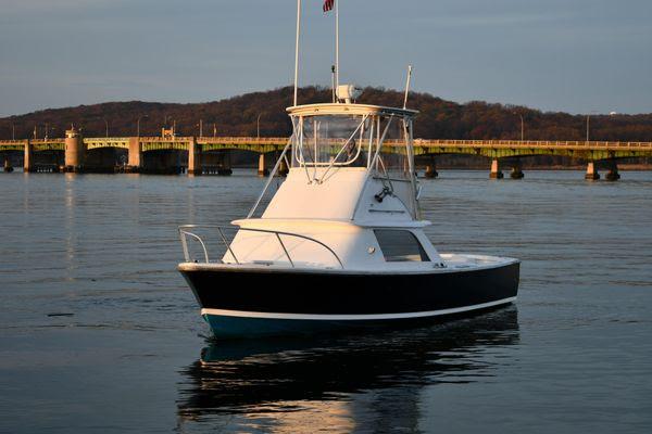 1965 Bertram Sportfisher boat on calm water near a bridge at sunset.