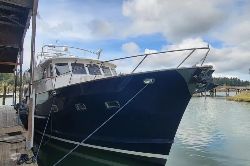 Fellowship Yacht Photos Pics 2001 Grand Alaskan Pilothouse yacht docked by a wooden pier under a cloudy sky.