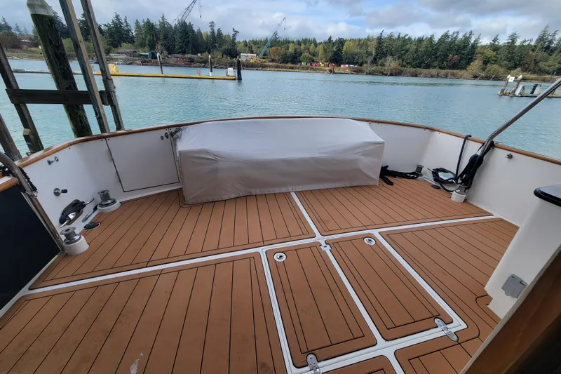 Fellowship Yacht Photos Pics 2001 Grand Alaskan Pilothouse boat deck with teak flooring, docked by a scenic waterfront.