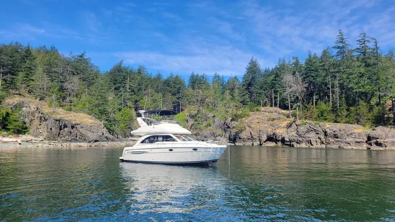 Queen Alexia Yacht Photos Pics 2005 Meridian 341 Sedan yacht on calm water, surrounded by lush forest and rocky shoreline.