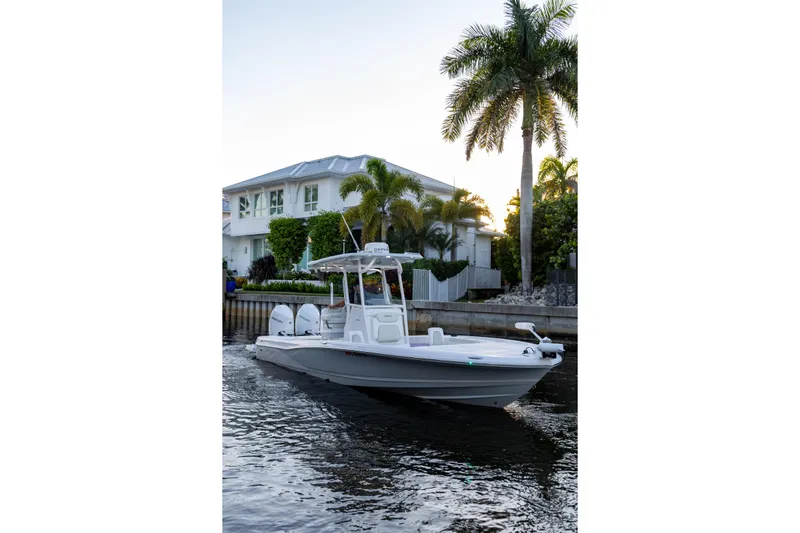  Yacht Photos Pics 2022 Caymas 28 HB Twin boat cruising near waterfront home with palm trees.