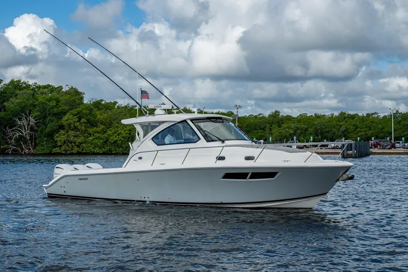  Yacht Photos Pics 2022 Pursuit OS 355 Offshore boat cruising on a calm waterway with lush greenery.