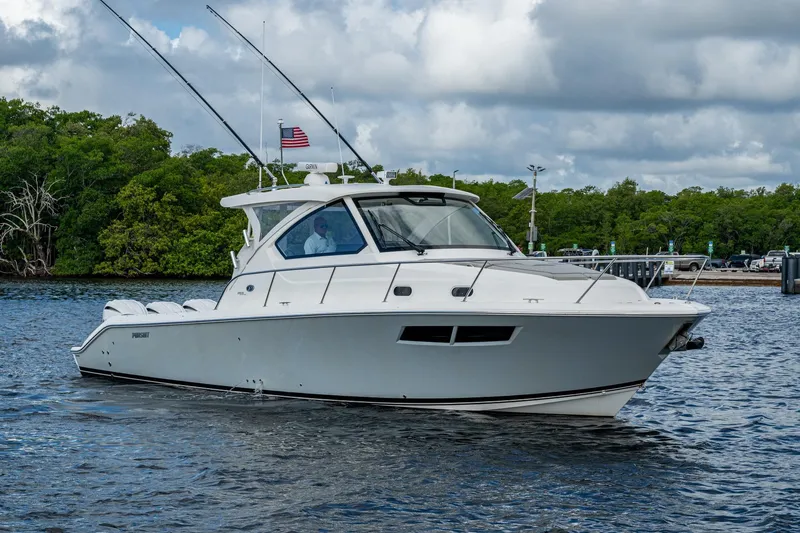  Yacht Photos Pics 2022 Pursuit OS 355 Offshore boat cruising on a calm waterway with lush greenery.