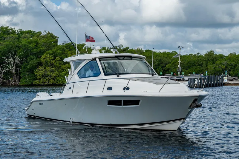  Yacht Photos Pics 2022 Pursuit OS 355 Offshore boat cruising on a calm waterway, surrounded by lush greenery.