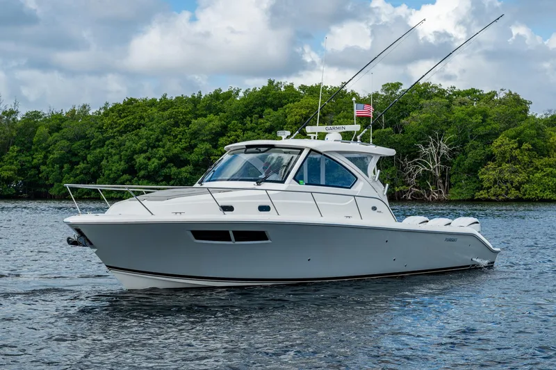  Yacht Photos Pics 2022 Pursuit OS 355 Offshore boat on water, surrounded by lush greenery.