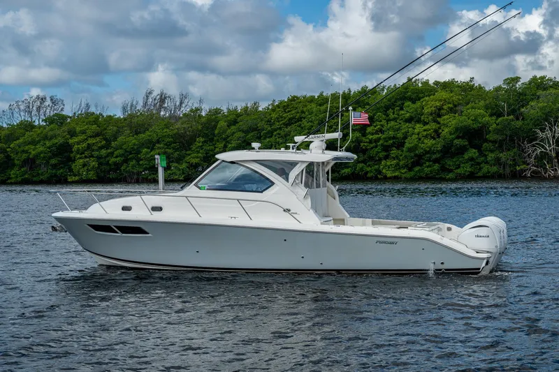  Yacht Photos Pics 2022 Pursuit OS 355 Offshore boat on water, surrounded by lush greenery.