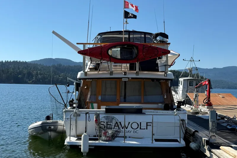Sea Wolf Yacht Photos Pics 1994 Bayliner 4788 Pilot House Motoryacht docked, featuring kayak and flags, in scenic bay.