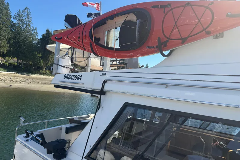 Sea Wolf Yacht Photos Pics 1994 Bayliner 4788 Pilot House Motoryacht with red kayak on deck, docked by the shore.