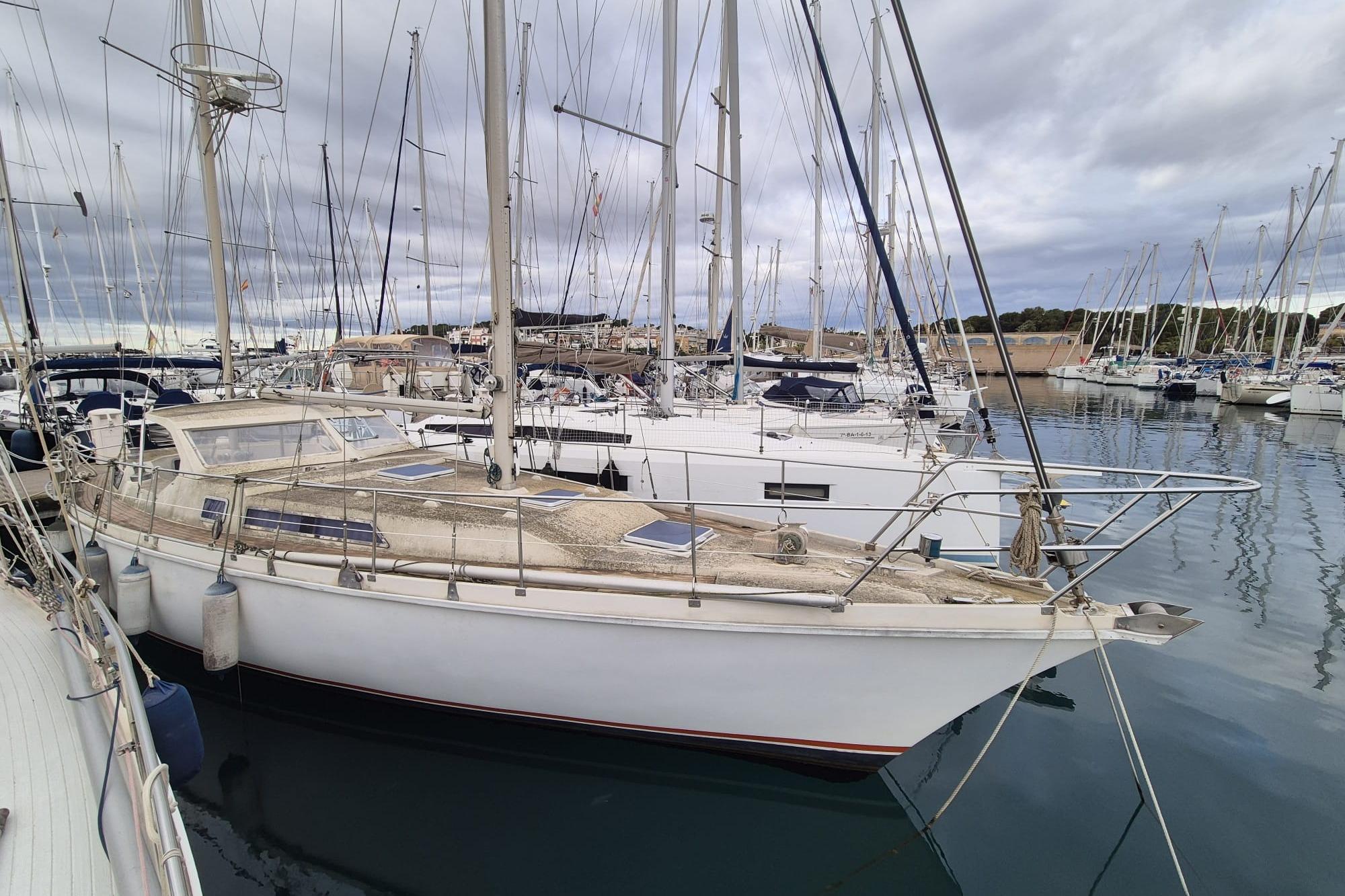 1980 Amel Sharki sailboat docked in a marina, surrounded by other boats.
