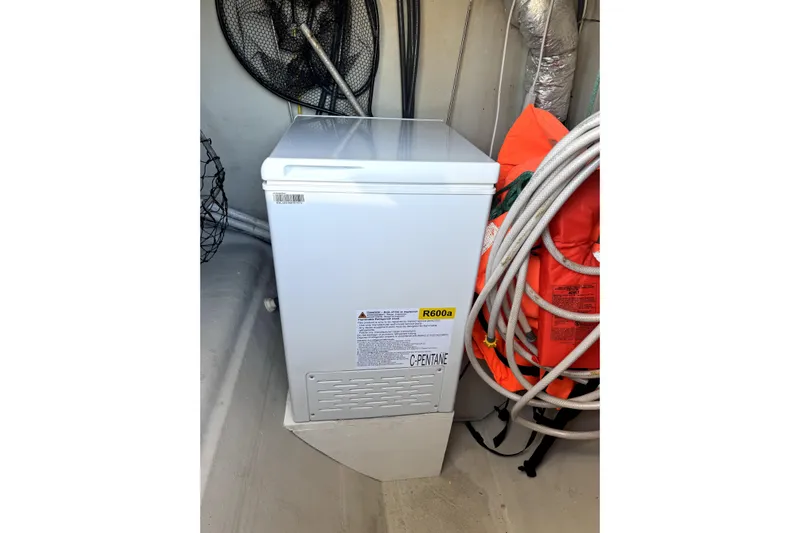 Who Cares Yacht Photos Pics White chest freezer in a boat storage area, surrounded by ropes and life jackets.