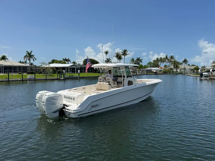  Yacht Photos Pics 2018 Boston Whaler 330 Outrage boat on calm water, clear sky, palm trees in background.