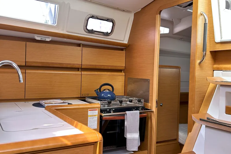 Patience Yacht Photos Pics Interior of 2012 Jeanneau Sun Odyssey 379 sailboat, featuring a compact kitchen with wooden cabinetry.