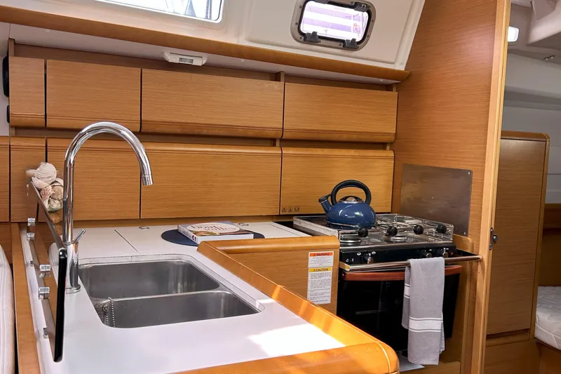 Patience Yacht Photos Pics Interior of 2012 Jeanneau Sun Odyssey 379 yacht kitchen with sink, stove, and wooden cabinets.