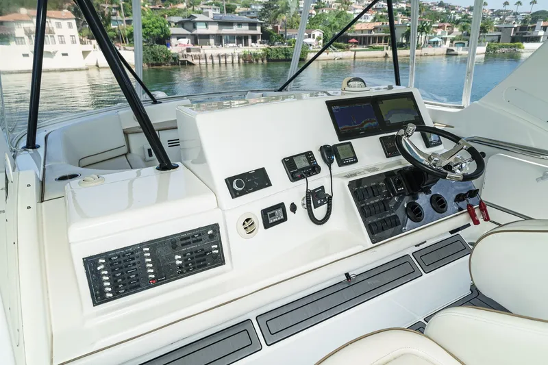 Nauti Pops Yacht Photos Pics 2007 Silverton Convertible yacht helm with navigation controls and steering wheel, docked by waterfront homes.