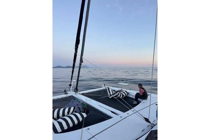 Pure Joy Yacht Photos Pics 2023 Seawind 1600 Passagemaker sailing at sunset with a person relaxing on deck.