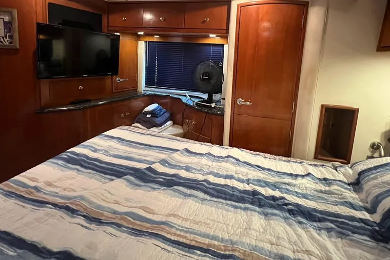 Kiki's Tiki Yacht Photos Pics Interior of 2000 Carver 506 Motor Yacht bedroom with striped bedding and wooden cabinetry.