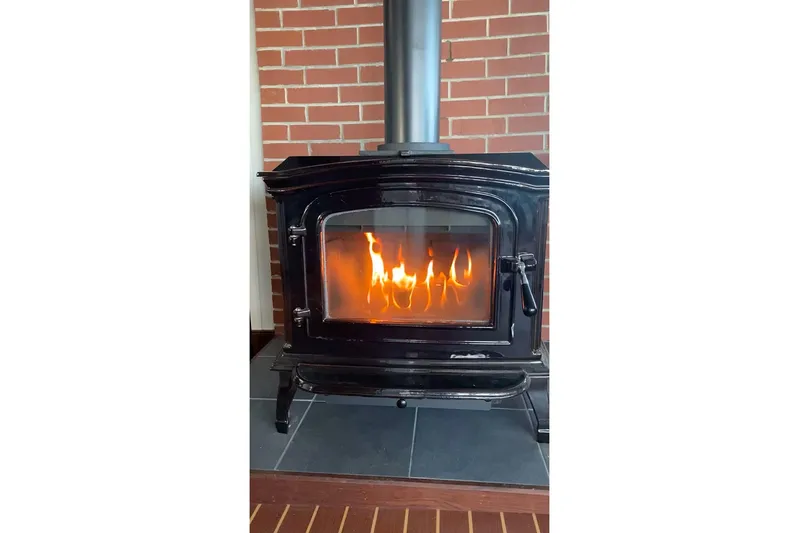 Anne S Pierce Yacht Photos Pics Black wood-burning stove with visible flames, set against a brick wall background.