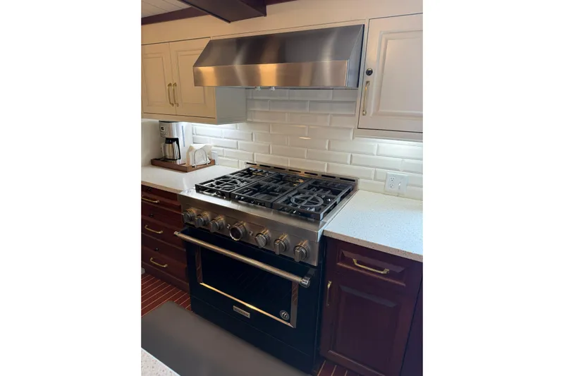 Anne S Pierce Yacht Photos Pics Modern kitchen with stainless steel stove, white cabinets, and custom backsplash, 2021 Glovertown Shipyard.