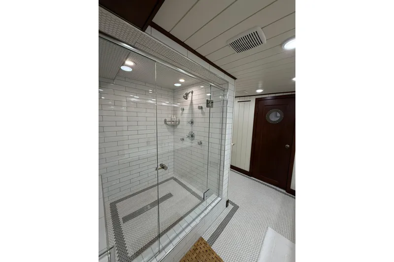 Anne S Pierce Yacht Photos Pics Luxurious ship bathroom with glass shower, white tiles, and wooden accents, Custom Glovertown Shipyard 2021.