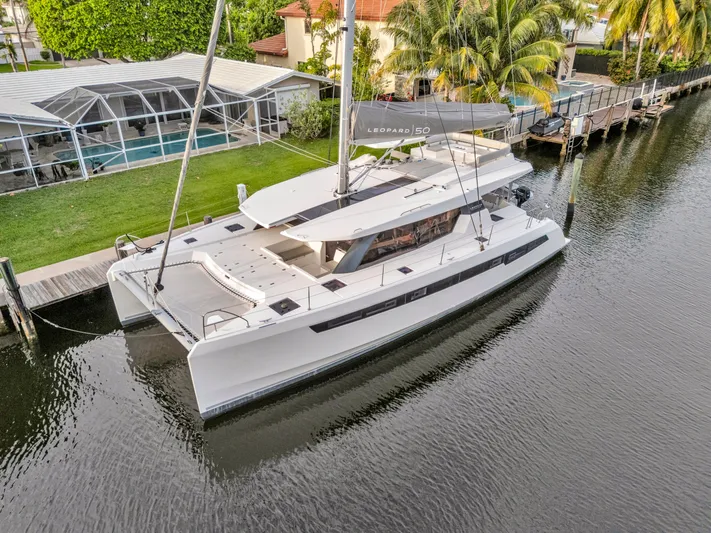  Yacht Photos Pics 2021 Leopard 50 catamaran docked by a canal, surrounded by lush greenery and a residential area.