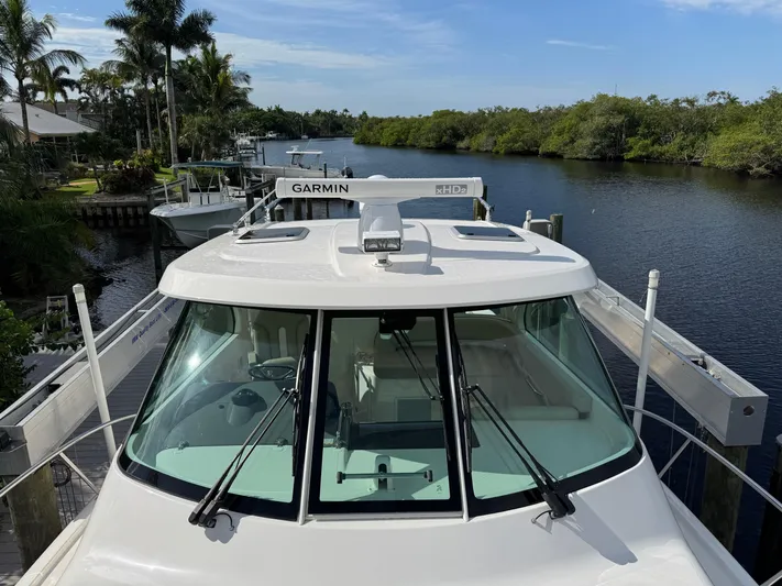  Yacht Photos Pics 2015 Pursuit OS 385 Offshore boat docked by a scenic waterway with lush greenery.